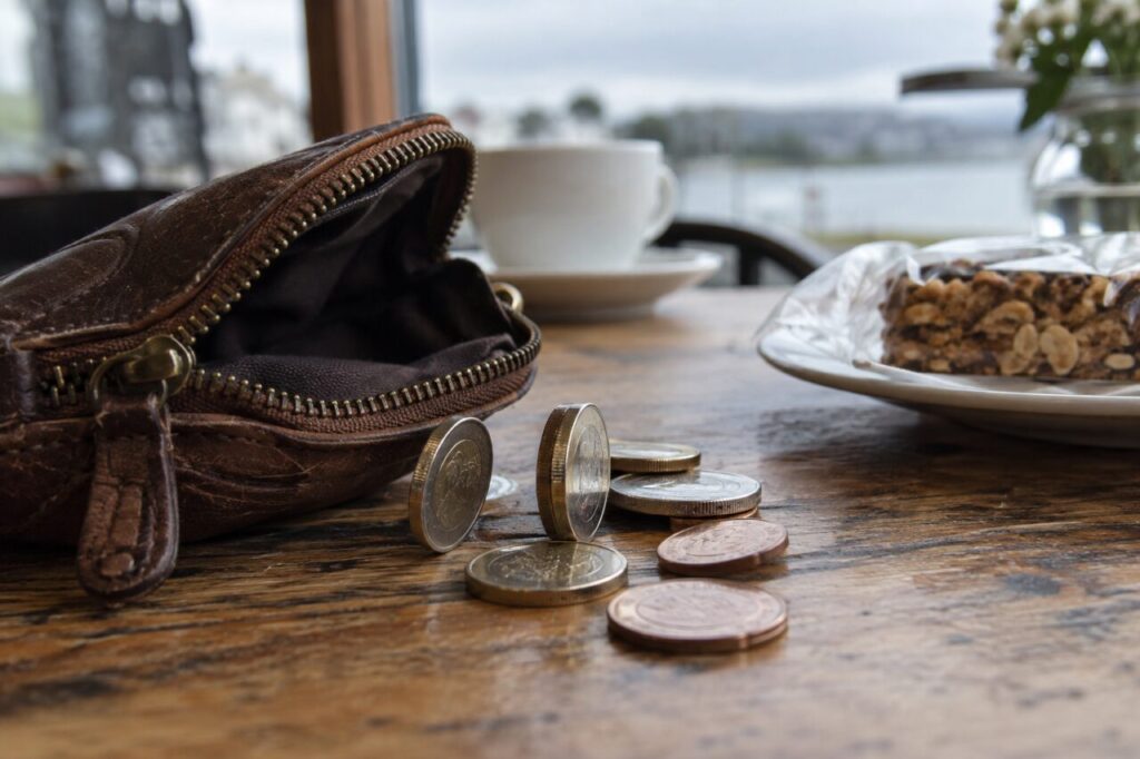 Coins beside an open leather purse with a packaged snack in the background